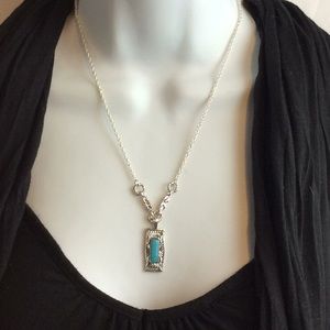 Silver tone necklace with a turquoise color .